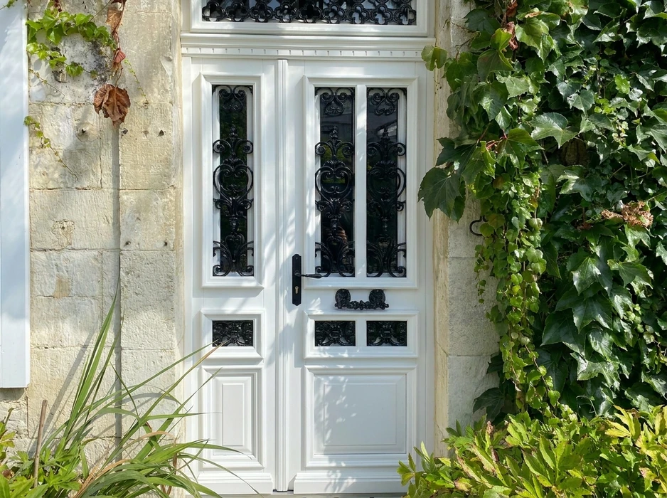 Porte d'entrée double vantaux blanche de style classique, encadrée de pierres calcaires et de lierre grimpant