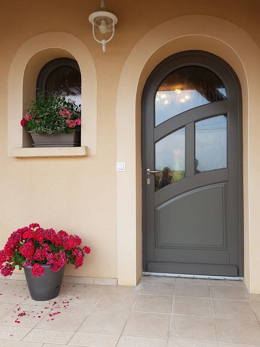 Entrée de maison élégante avec une porte d'entrée cintrée gris anthracite, vitrage transparent asymétrique à traverses courbes, poignée dorée