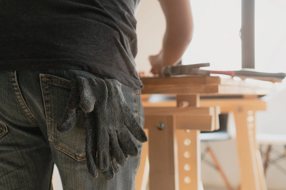 Un artisan dans un atelier moderne de menuiserie d'extérieur, travaillant sur la fabrication d'une fenêtre aluminium ou d'un volet motorisé sur établi, utilisant des outils professionnels spécialisés. L'atelier doit montrer des éléments caractéristiques de la menuiserie contemporaine (profilés aluminium, menuiseries en cours de fabrication, équipements modernes). L'artisan porte des vêtements professionnels (pas de costume folklorique). La scène reflète la fabrication sur mesure de fermetures modernes en atelier français.