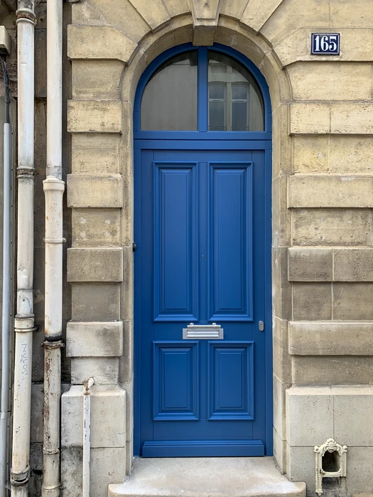 Entrée de maison élégante avec une porte d'entrée cintrée gris anthracite, vitrage transparent asymétrique à traverses courbes, poignée dorée