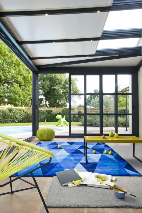 Intérieur lumineux avec fenêtre double vantail à oscillo-battant, cadre bois naturel, ouvrant sur terrasse dallée et jardin verdoyant