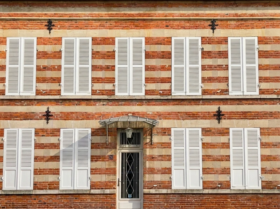 Façade extérieure d'une maison avec quatre fenêtres à guillotine équipées de volets battants en bois peints en vert sauge