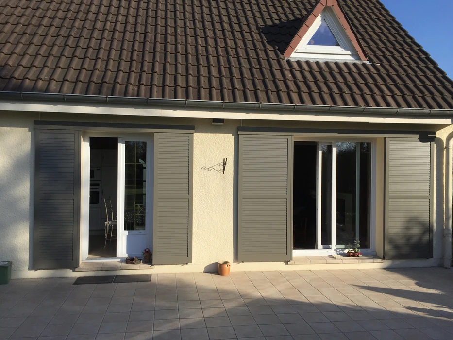 Façade extérieure d'un bâtiment résidentiel en crépi beige, équipée de deux fenêtres PVC blanc avec volets roulants motorisés