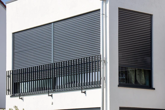 Façade moderne d'une maison contemporaine avec volets roulants métalliques, baies vitrées coulissantes et terrasse en bois
